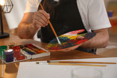 Young man with painting tools at table in artist studio, closeup