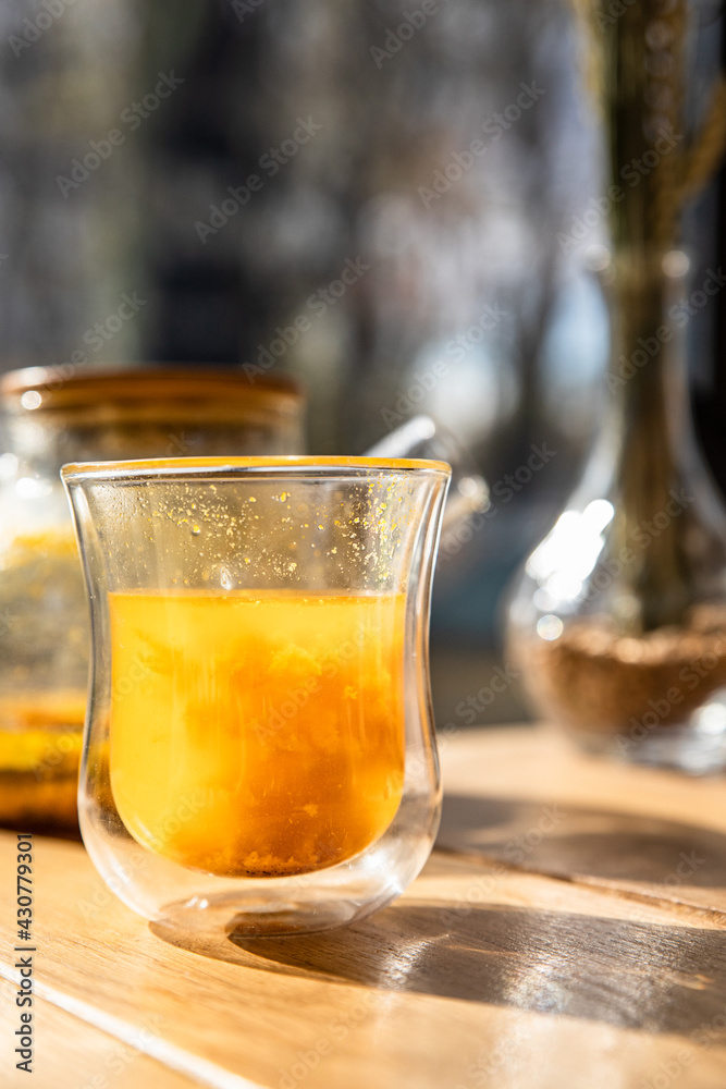 Glass cup with sea buckthorn tea and teapot on wooden table in cafe. Traditional autumn hot drink. Glass cup with sea buckthorn tea and teapot on wooden table in cafe. Traditional autumn hot drink.