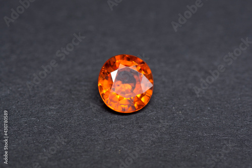 Genuine natural mined loose oval faceted mandarin orange bright deep saturated color spessartine garnet gemstone setting for making jewelry. Transparent semiprecious stone on gray background. photo