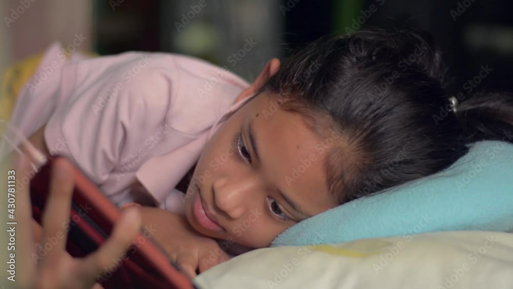 Happy Asian pretty girl wearing earphone watching social video or movie series TV from mobile phone while lying on the bed at home. Digital entertainment from smartphone. Happy Asian pretty girl wearing earphone watching social video or movie series TV from mobile phone while lying on the bed at home. Digital entertainment from smartphone.