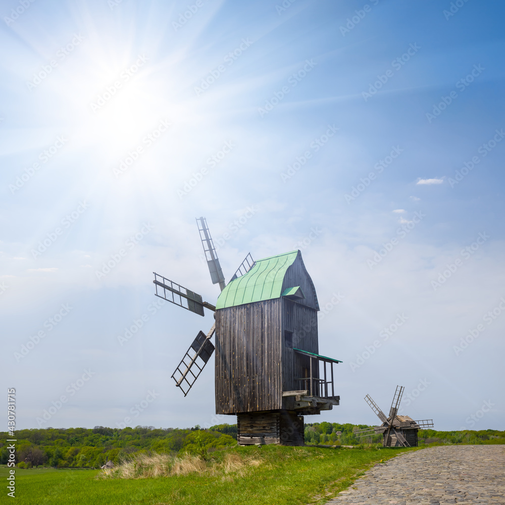 Naklejka premium wooden authentic windmill among green fields at the sunny day, historical farm scene