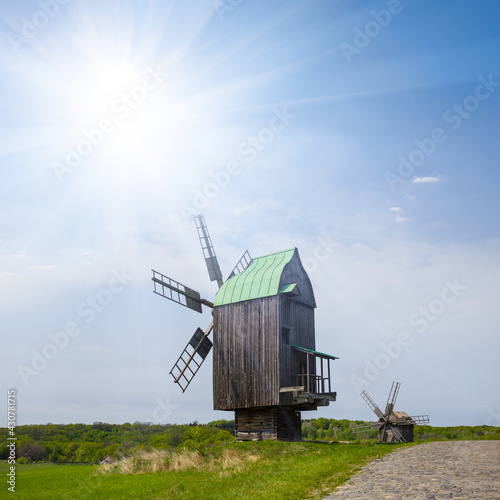 wooden authentic windmill among green fields at the sunny day, historical farm scene
