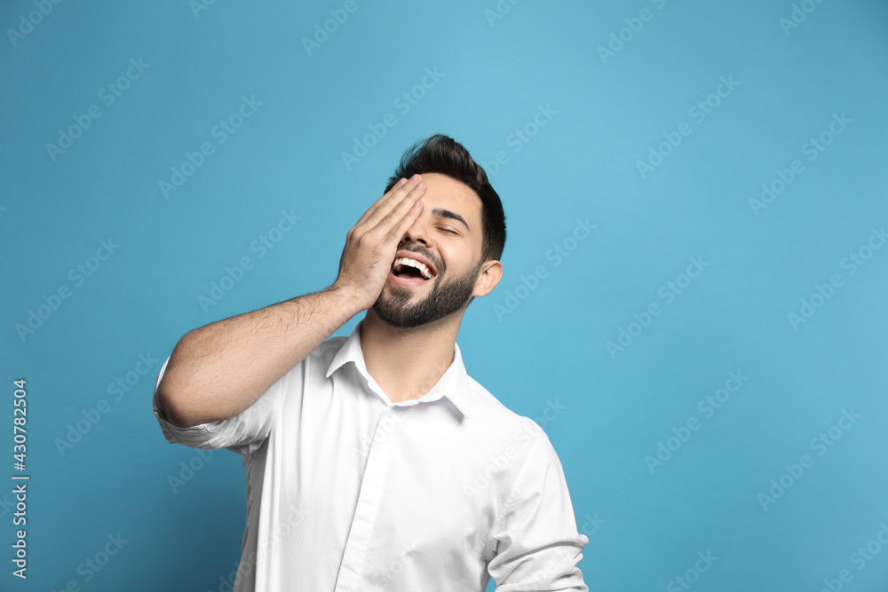Young man laughing on light blue background. Funny joke Young man laughing on light blue background. Funny joke