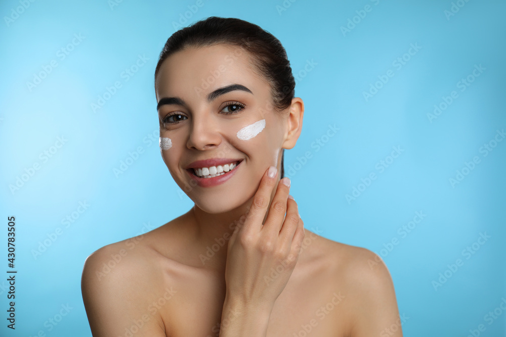 Young woman applying facial cream on light blue background Young woman applying facial cream on light blue background