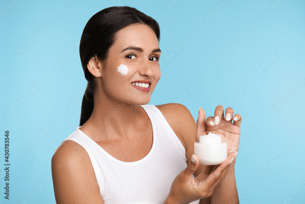 Young woman applying facial cream on light blue background Young woman applying facial cream on light blue background