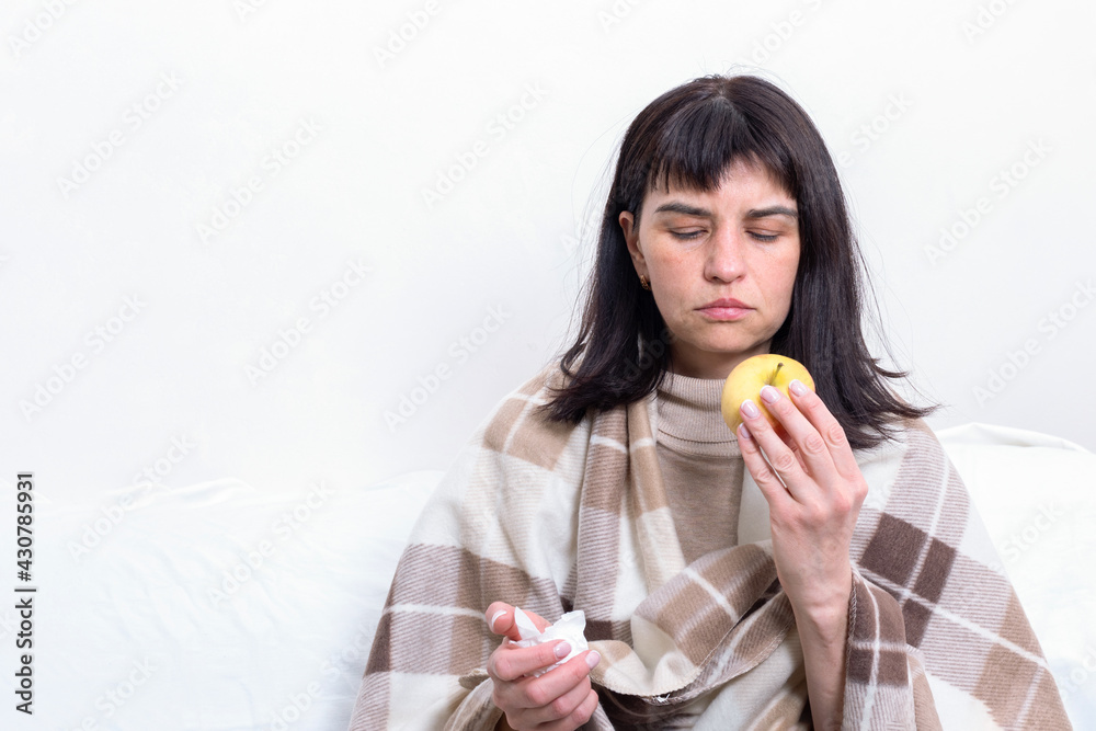 Portrait of a sick attractive woman wrapped in a blanket holding an apple. The girl is at home in quarantine Portrait of a sick attractive woman wrapped in a blanket holding an apple. The girl is at home in quarantine