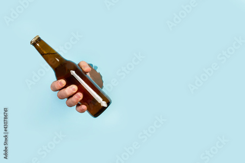 Mano de hombre sosteniendo una botella de cerveza a traves de un agujero en un papel celeste. Vista de frente. Copy space