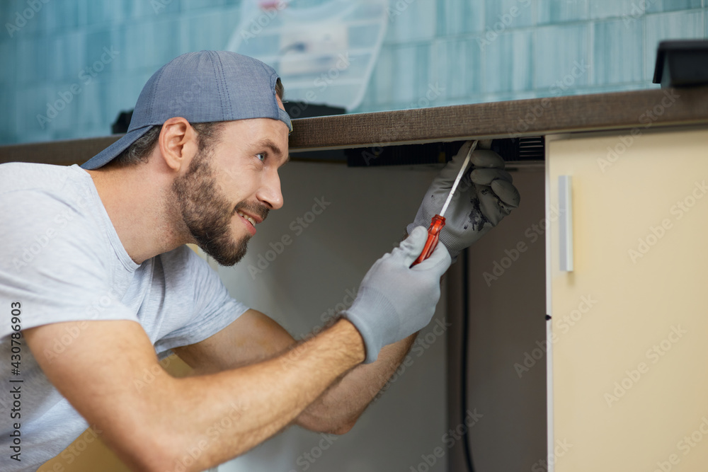 Doing it right. Portrait of young repairman, professional plumber looking concentrated while fixing sink pipe in the kitchen indoors Doing it right. Portrait of young repairman, professional plumber looking concentrated while fixing sink pipe in the kitchen indoors