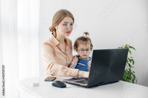 Young woman works at home using a laptop. A small kid is sitting in her mother's arms. Work on maternity leave