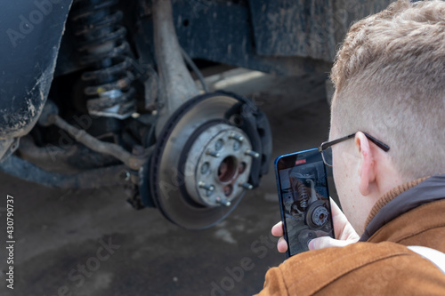 A man takes a video on his phone about the hydraulic brake of a passenger car. The brake disc is blurred, the man is focused