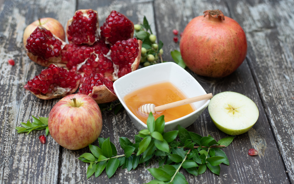 Creative layout of traditional symbols for jewish holiday - apples, cup with honey, pomegranate, green branch on wooden background. Concept Rosh Hashanah tova jewish New Year. Top view, fresh fruits Creative layout of traditional symbols for jewish holiday - apples, cup with honey, pomegranate, green branch on wooden background. Concept Rosh Hashanah tova jewish New Year. Top view, fresh fruits