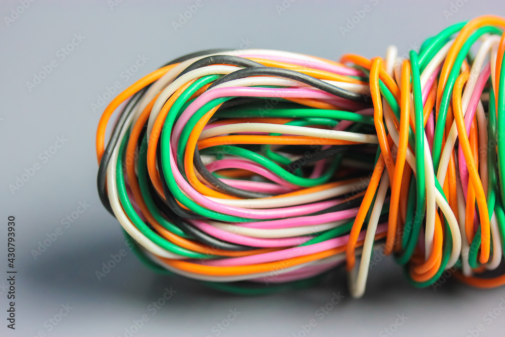 A bundle of multicolored electrical, car, computer, telephone wires twisted together background. Orange, green, pink, white cables on grey background . Computer networks, electrician services concept.