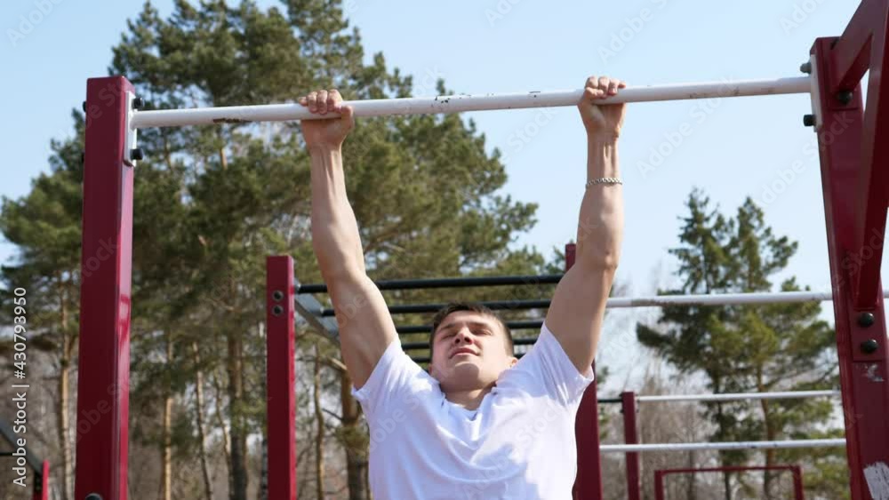 Young man doing pull-ups on the horizontal bar while training outdoors. Active person, health care, strong hands Young man doing pull-ups on the horizontal bar while training outdoors. Active person, health care, strong hands