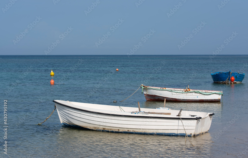 On the coast of the Mediterranean there are three small, empty, old fishing boats under a blue sky
