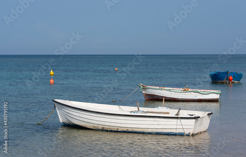 On the coast of the Mediterranean there are three small  empty  old fishing boats under a blue sky