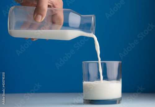 glass of milk half full, hand with overturned glass bottle, blue background