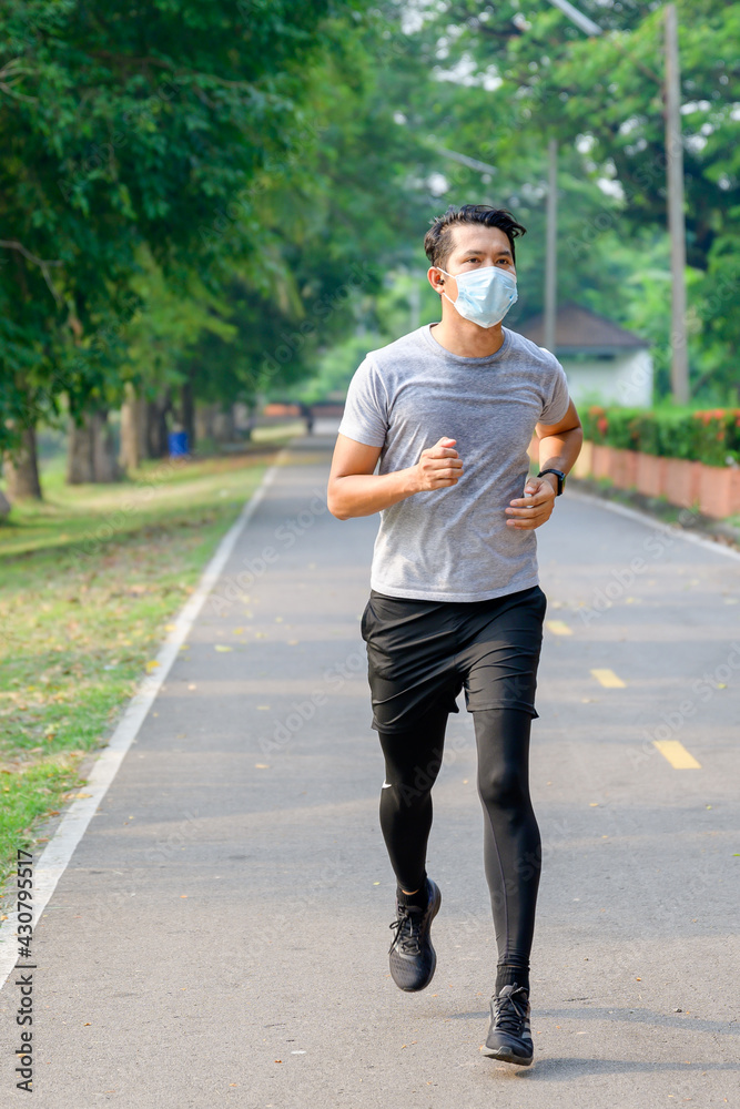 Young asian man Wear a fitness mask Run in the park Sweating from a morning workout concept: wear a mask against SARS-Cov-2.