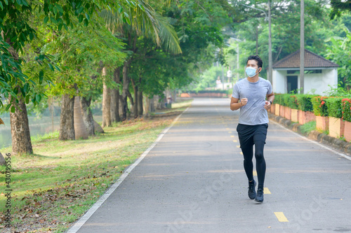 Young asian man Wear a fitness mask Run in the park Sweating from a morning workout concept: wear a mask against SARS-Cov-2.