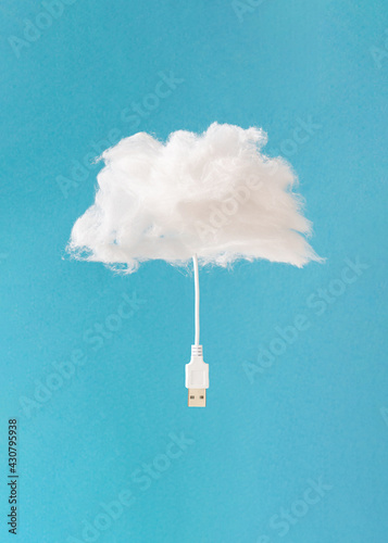 Minimal composition with soft fluffy cloud and computer connection cable against sky blue background. Creative cloud storage symbol.