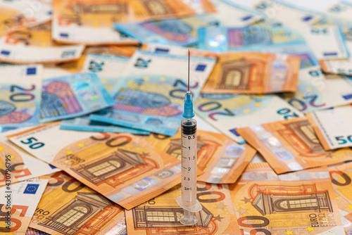 spread stack of Euro banknotes with syringe on top of them  health costs concept