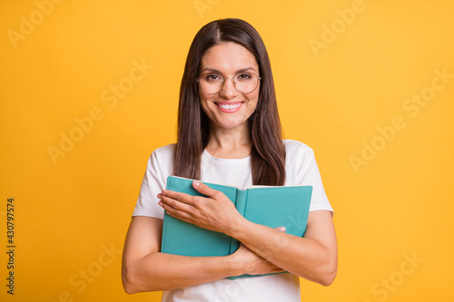 Portrait of attractive cheerful intellectual woman hugging reading book isolated over bright yellow color background
