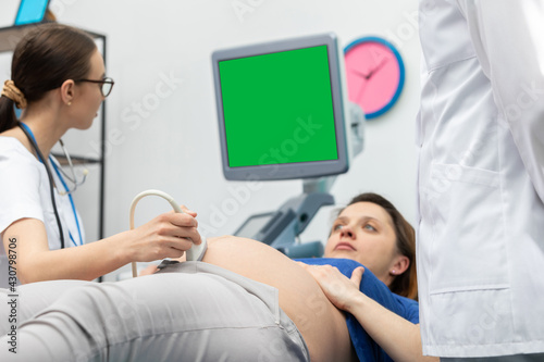 A lady doctor checks the abdomen of a pregnant patient with an ultrasound. Gynecology office.