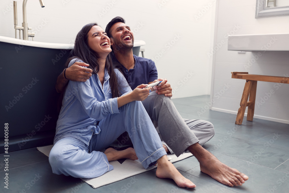 Excited Couple Sitting On Floor In Bathroom At Home With Positive Home Pregnancy Test Excited Couple Sitting On Floor In Bathroom At Home With Positive Home Pregnancy Test