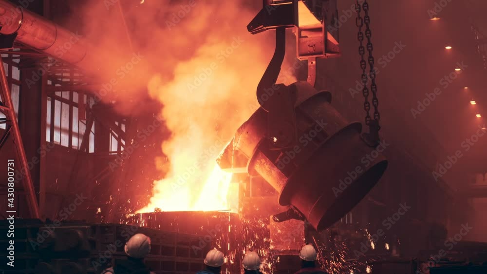 Molten metal pour from big container Into sand mold with many sparks. Iron casting in metallurgy foundry plant, heavy industry.