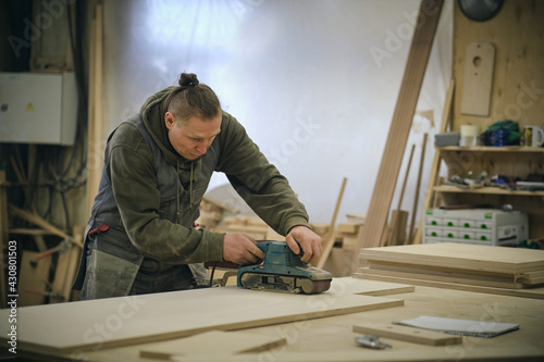 Close up. Carpenter at workshop polishes wooden board with a electric orbital sander. Woodwork and furniture making concept.