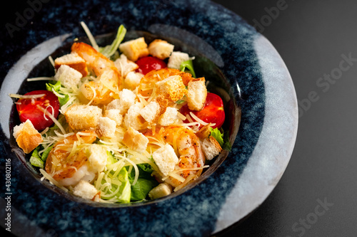 Fresh caesar salad with grilled chicken in a served plate on a black background.
