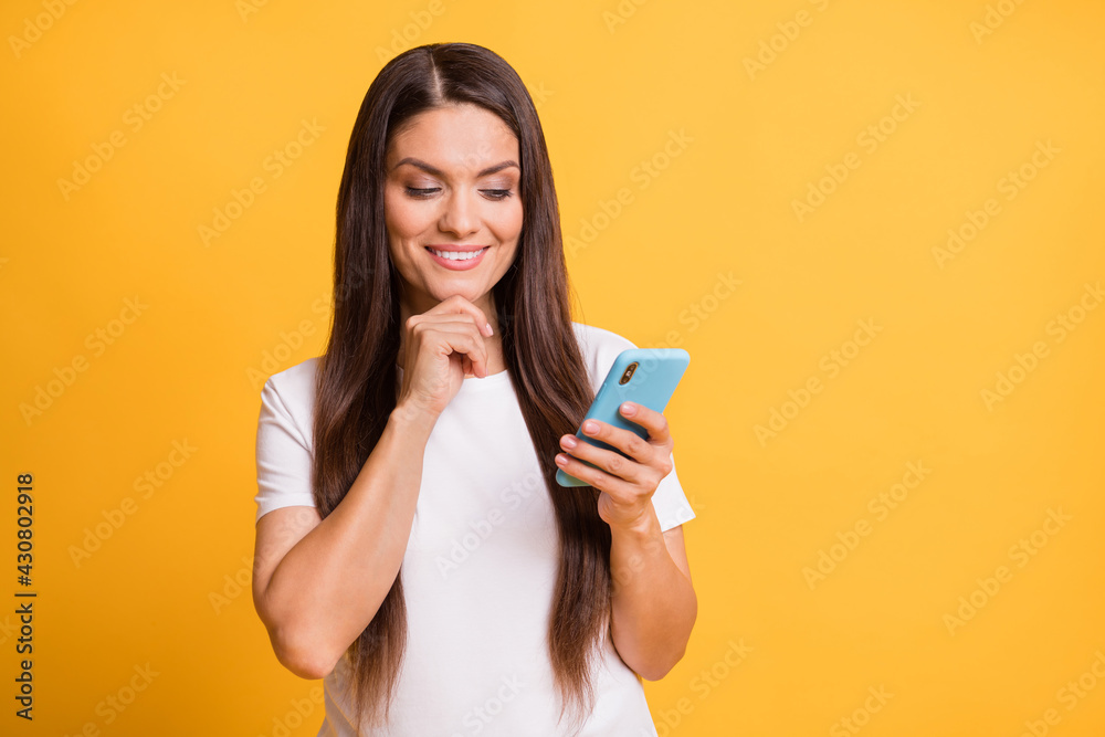 Photo portrait of thoughtful woman using app smartphone social media smiling isolated on vibrant yellow color background Photo portrait of thoughtful woman using app smartphone social media smiling isolated on vibrant yellow color background