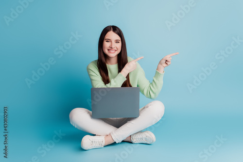 Young happy woman holding laptop point index finger empty space isolated over blue background © Tetiana