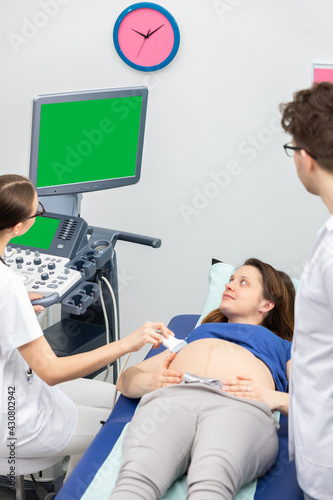 A nurse performs an ultrasound on a pregnant patient under the guidance of the attending doctor. Green screen.