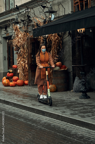 A girl rides an electric scooter in the city in autumn. Use of environmentally friendly personal transport.
