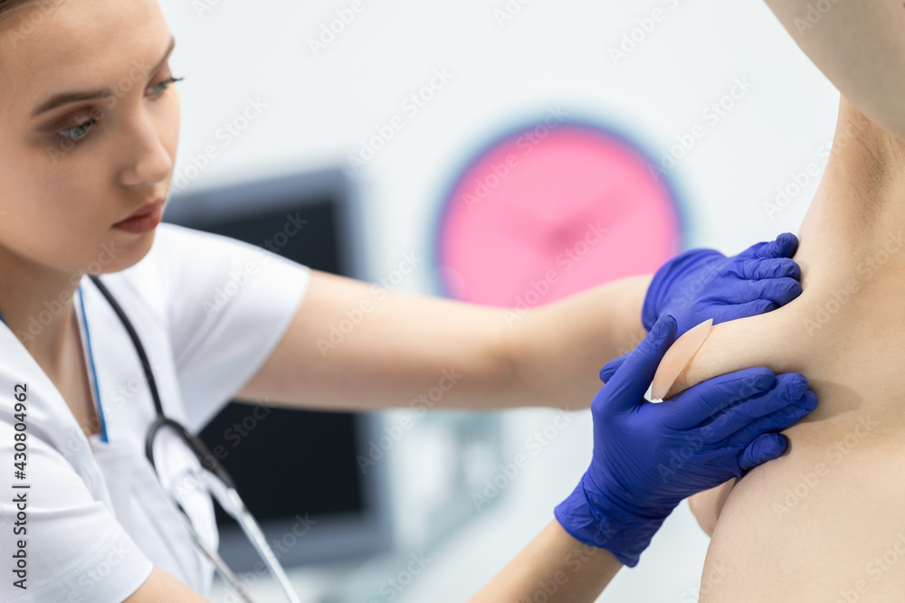 The doctor conducts a breast exam on a young patient, gently applying pressure with her hands. Close-up view.
