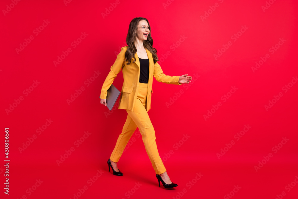 Full length body size view of attractive chic slim cheerful lady walking carrying laptop isolated over vivid red color background Full length body size view of attractive chic slim cheerful lady walking carrying laptop isolated over vivid red color background