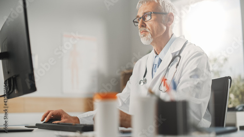 Wallpaper Mural Experienced Middle Aged Male Doctor Wearing White Coat Working on Personal Computer at His Office. Senior Medical Health Care Professional Working with Test Results, Patient Treatment Planning. Torontodigital.ca