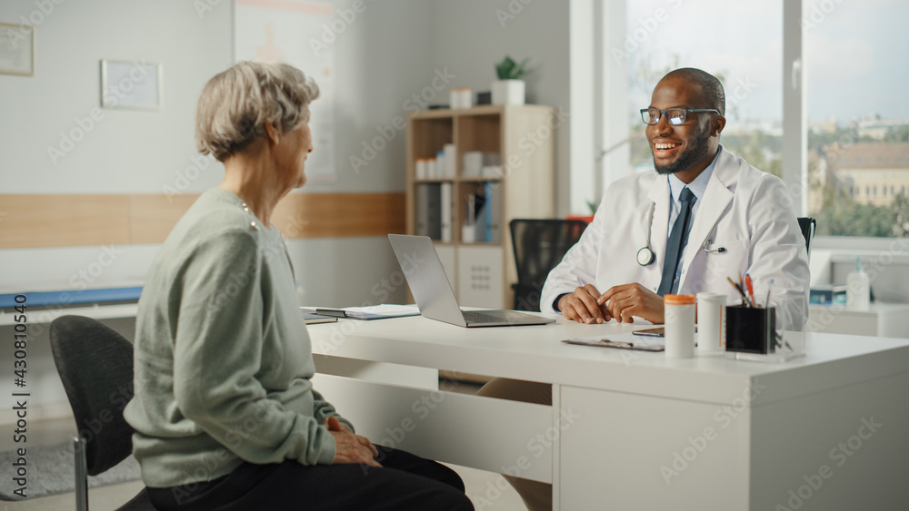 Obraz premium African American Family Doctor is Prescribing Medication to Senior Female Patient and Speaking with Her During Consultation in a Health Clinic. Physician Sitting Behind a Desk in Hospital Office.