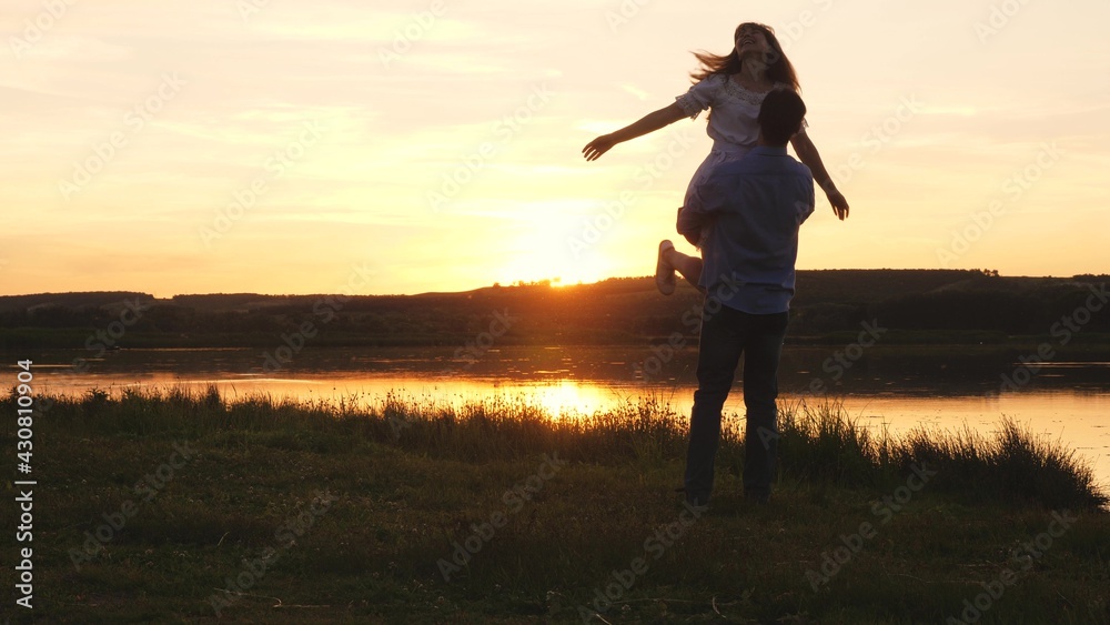 Family dancing at sunset on beach. Free people. Happy young woman jumps into arms of her beloved man. A loving couple man and woman dancing in bright rays of sun on background of lake.