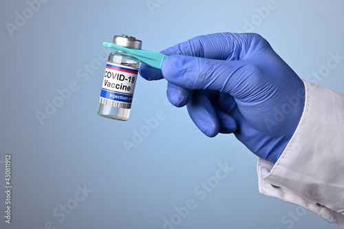 Doctor hand holds Covid-19 vaccine jar with plastic pincet. Hand in blue glove offers medical treatment against Covid virus. Vaccines are effective in preventing coronavirus and flu breakouts.
