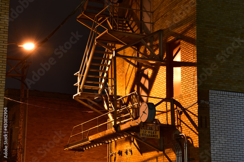 Tablou canvas Building fire escape in alley at night with windowlight and shadows