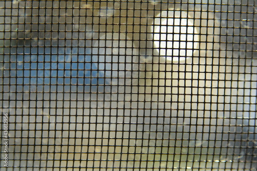 Macro image of window screen with out of focus lights outside creating distorted light shapes.