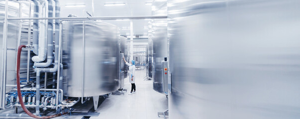 Worker female engineer operator in uniform uses process control panel food factory production line and steel tanker