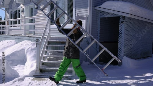 Slow motion shooting of a long haired young man placing an extensible professional ladder on the edge of a roof for a snow removal operation.