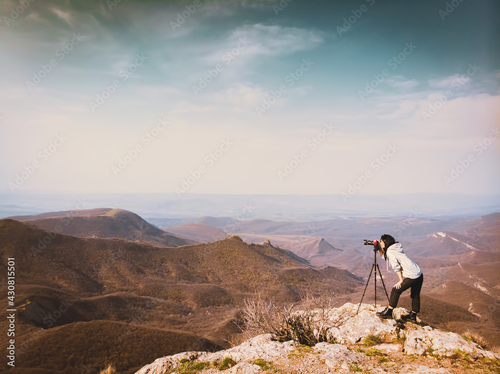 Side view young attractive caucasian hipster woman content creator photographing mountains with red girly DSLR camera on tripod