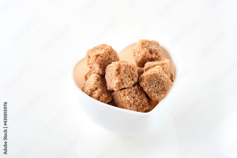 Cane sugar cubes in a white bowl isolated on white background. Selective focus. Cane sugar cubes in a white bowl isolated on white background. Selective focus.