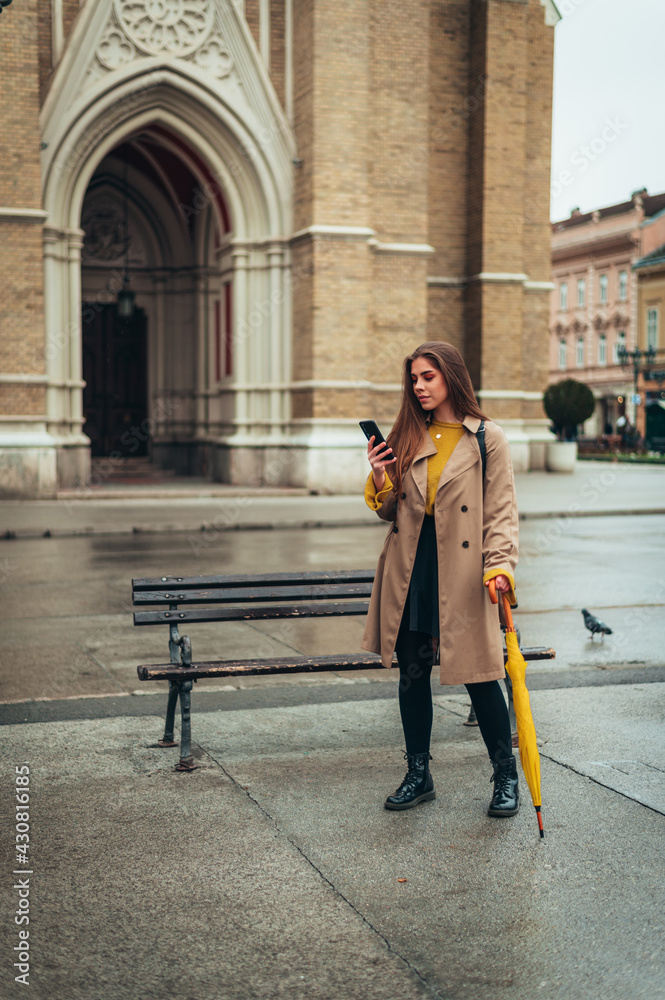 Woman using a smartphone and holding a yellow umbrella outside