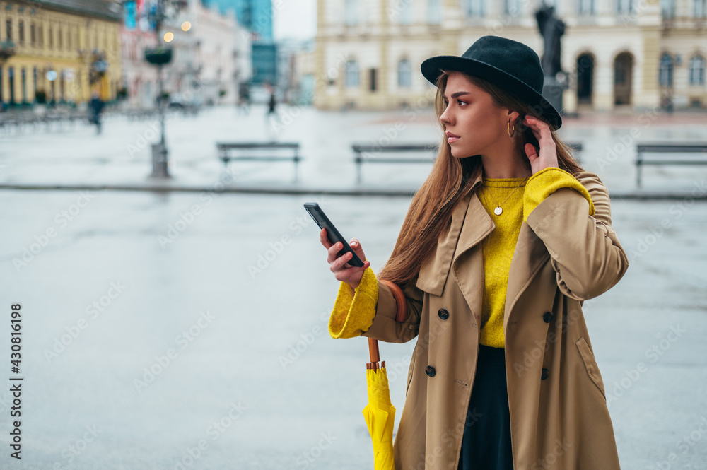 Fototapeta premium Woman using a smartphone and holding a yellow umbrella outside