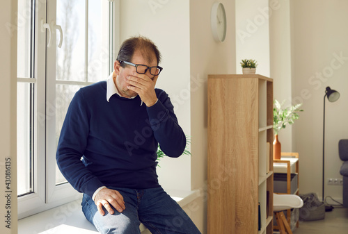 Fotografia Desperate senior man crying sitting alone on windowsill, trying to overcome grief or accept bad news