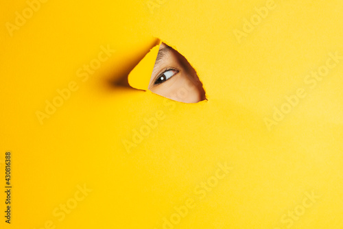 The boy peeks through a cut hole in the yellow paper wall. Human eye closeup.